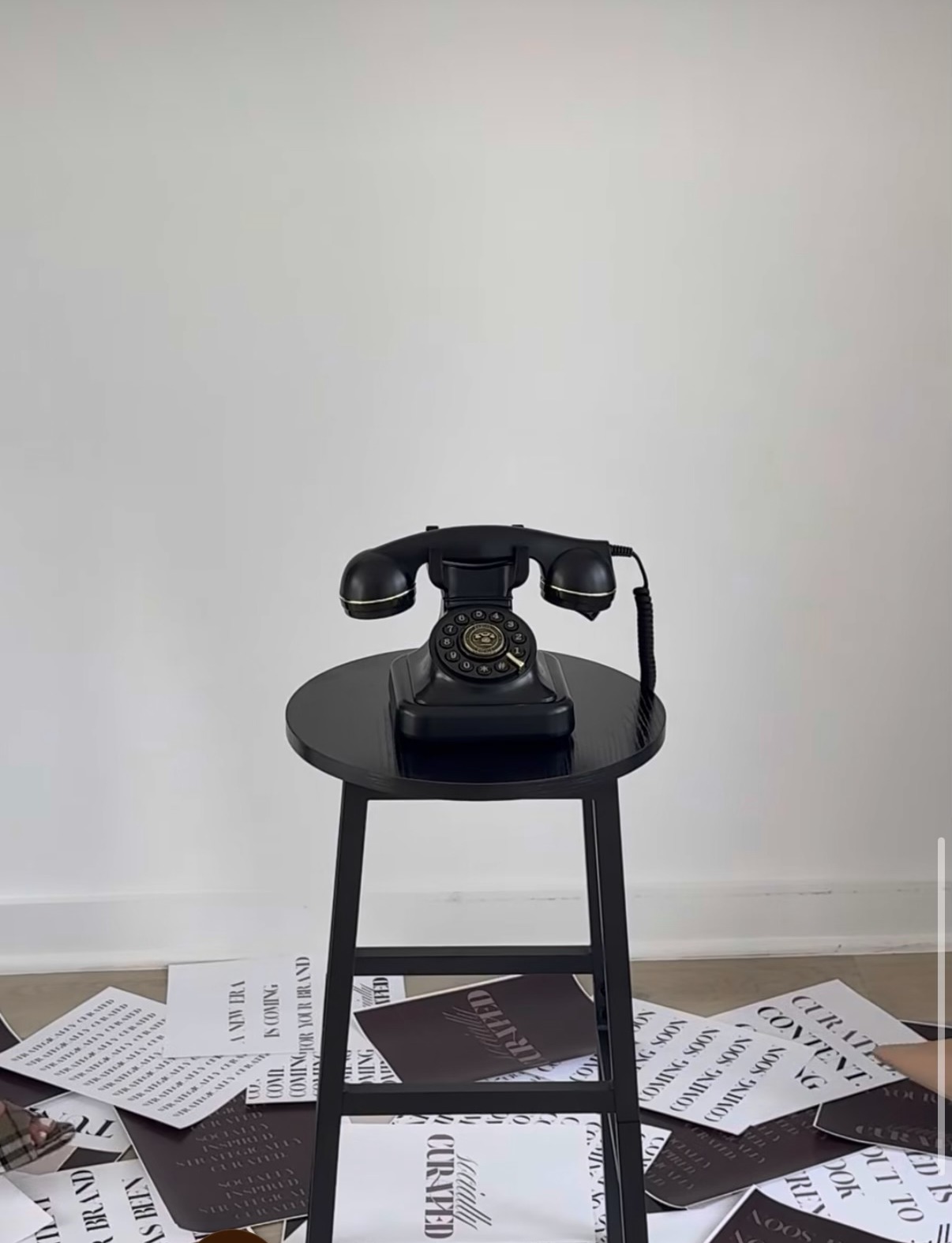 A black rotary phone on a black stool, surrounded by scattered Socially Curated launch cards